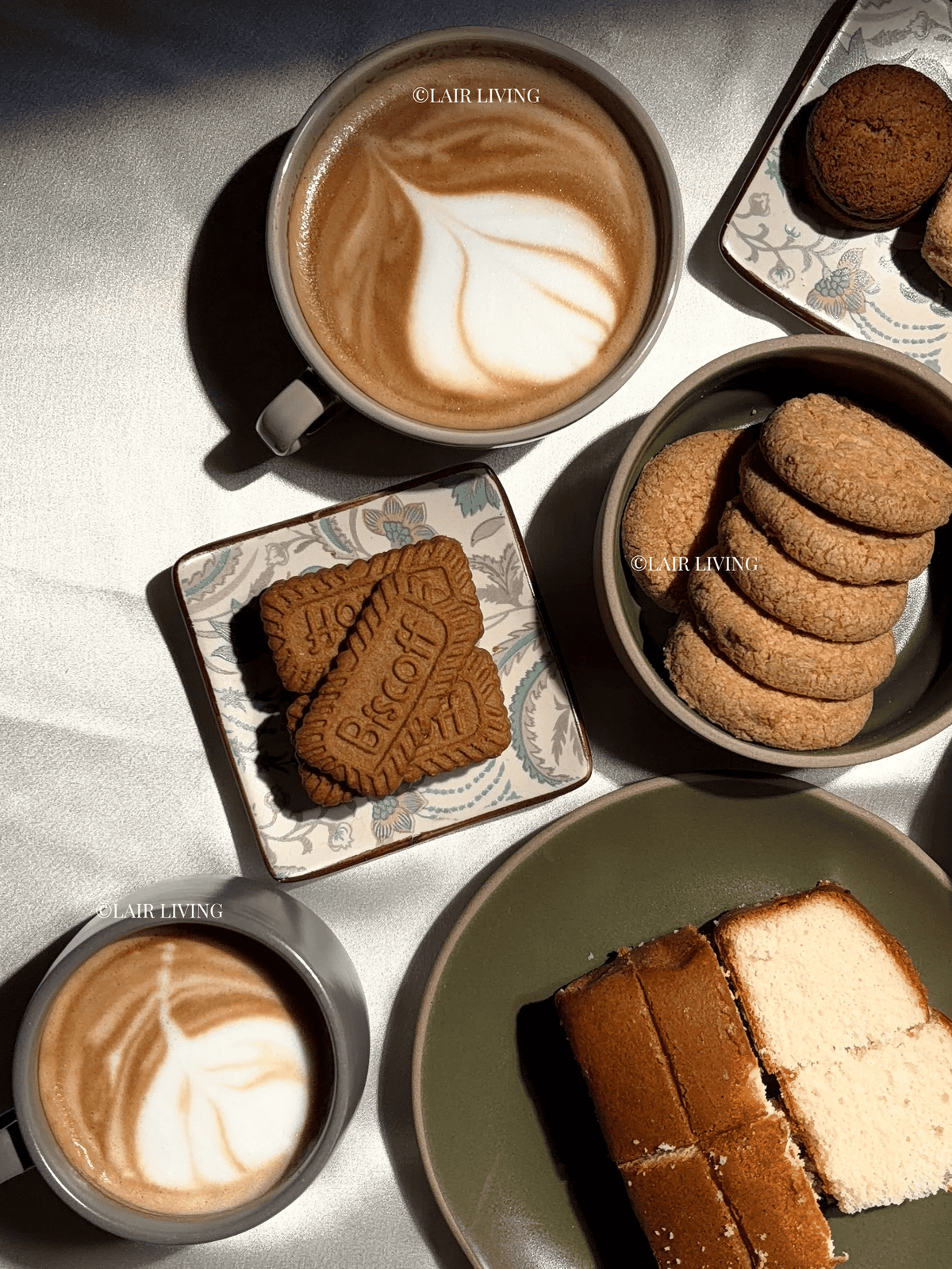 Coffee table spread with two Ashen cappuccino cups of latte art, biscuits and cake on Lair Living stoneware