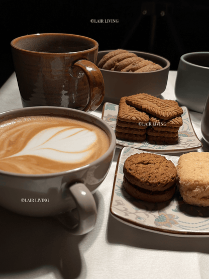 Ashen cappuccino cup filled with a latte and rosetta art, styled with biscuits on a ceramic platter — Lair Living