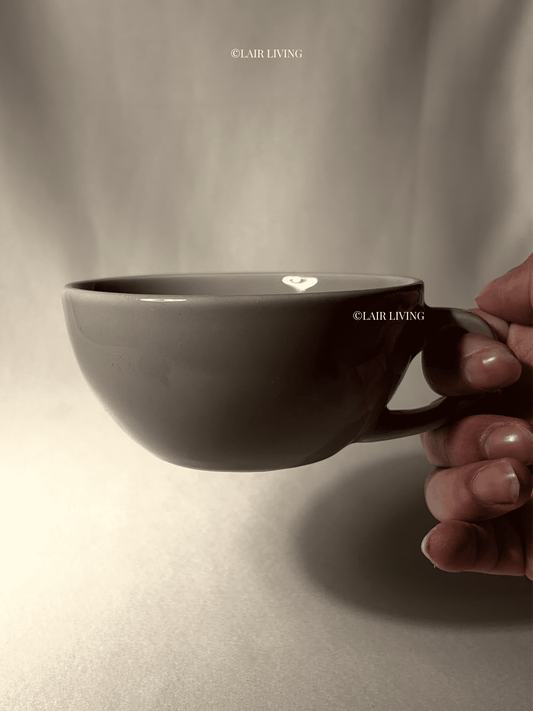 Hand holding the Ashen cappuccino cup, showing its wide shallow profile and compact handle — Lair Living handmade ceramic